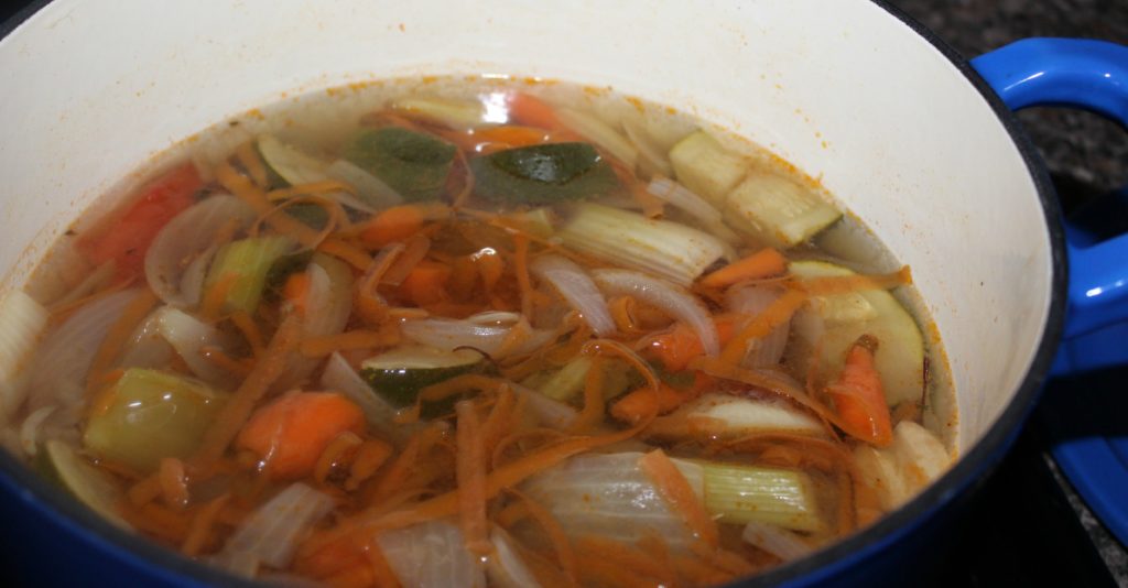 Step two of recipe with vegetable scraps, onion and diced tomatoes cooling in pot.