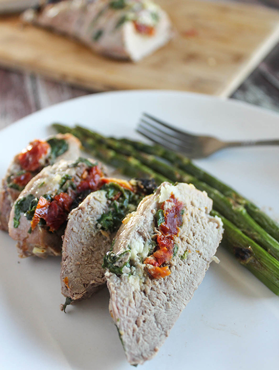 a close up photo of hasselback pork tenderloin sliced on a plate with asparagus.