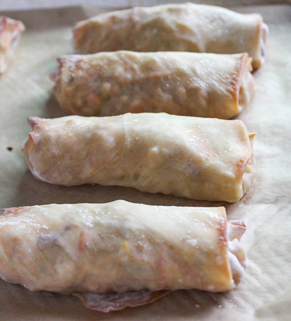 baked stuffed egg rolls lined up on a baking sheet