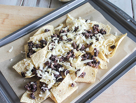 chips topped with beans and cheese on a baking sheet