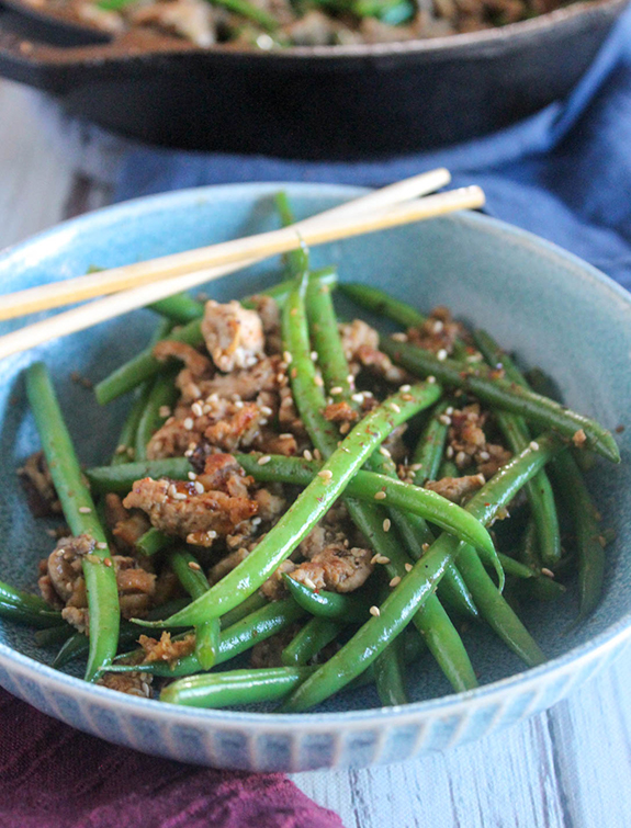 Image is of blue bowl with finished Spicy stir-fried pork and green beans. Chop sticks are resting on the side of the bowl.