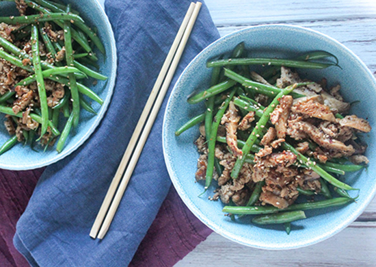 spicy green beans and pork with mushrooms in a bowl sprinkled with sesame seeds