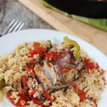 a boneless pork chop topped with tomatoes, peppers and onions over rice on a white plate