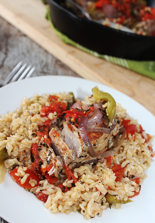 a boneless pork chop topped with tomatoes, peppers and onions over rice on a white plate