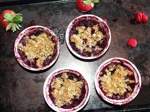 This images shows the cooked mixed berry crumbles on baking sheet with strawberries and raspberries.