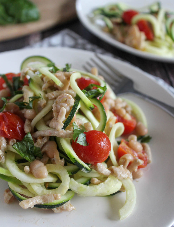 a close up picture of zucchini noodles with white beans on a plate