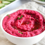 a close up picture of beet hummus in a whitte bowl