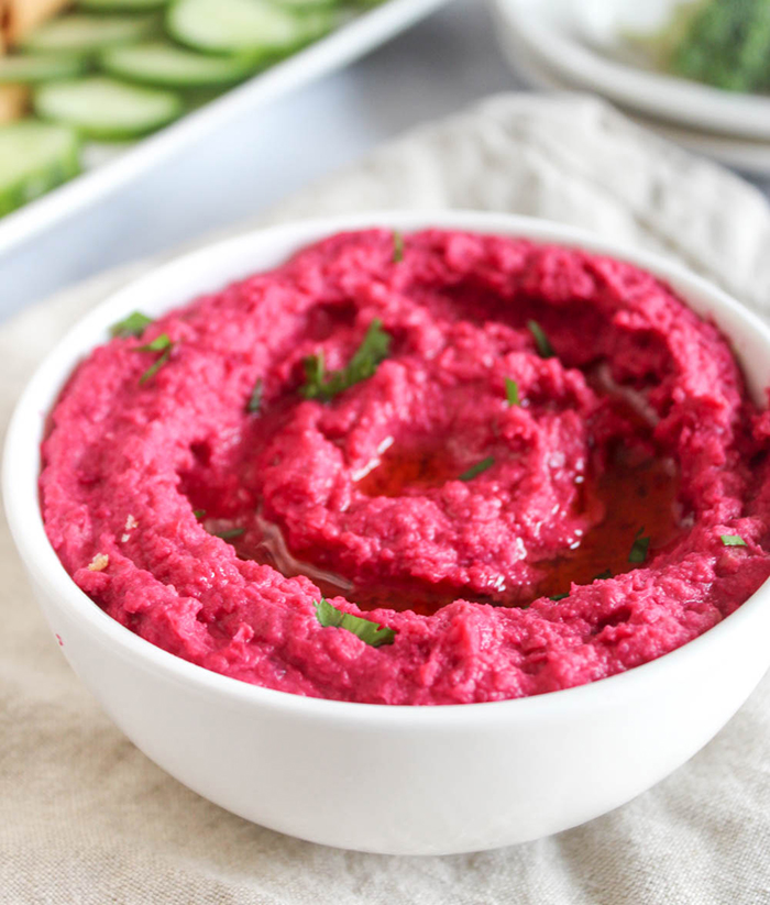 a close up picture of beet hummus in a whitte bowl
