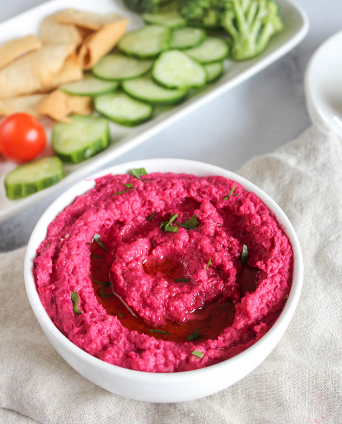 roasted beet hummus in a white bowl with a tray of fresh vegetables in teh background