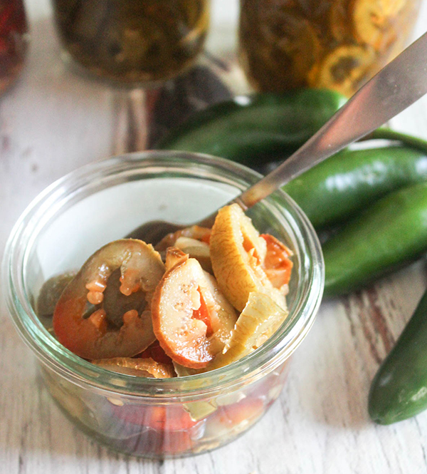 un frasco abierto de chiles jalapeños en escabeche con una cuchara