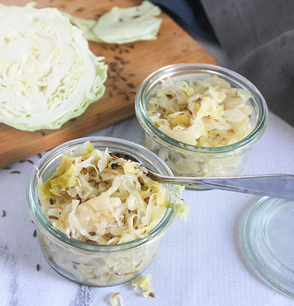 two jars of sauerkraut and a head of cabbage in the background