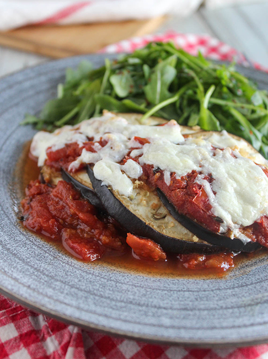 a close-up shot of eggplant parmesan on a blue plate with arugula