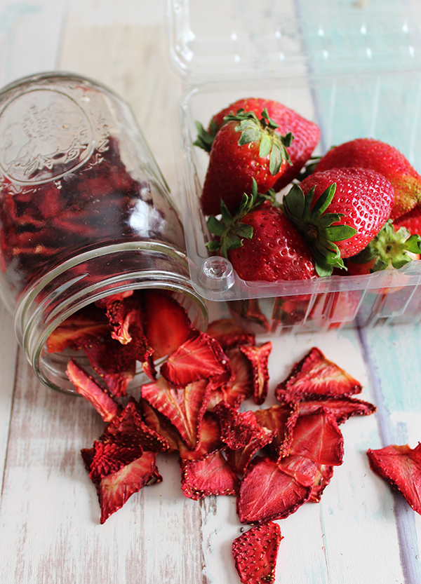 a jar of dehydrated strawberries next to fresh strawberries on a table