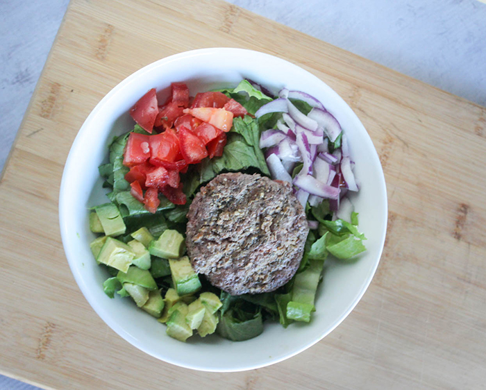 an overhead view of the burger bowl with a burger, lettuce tomatoes and onions