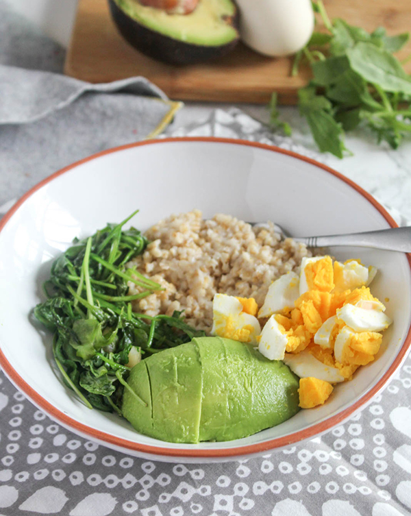 healthy savory breakfast bowl with sauteed greens oats eggs and avocado in a bowl