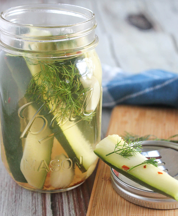 zucchini refrigerator pickle on a fork with a jar behind it