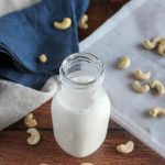 cashew milk in a milk bottle surrounded by cashews