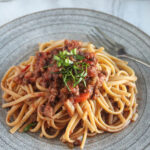 spaghetti covered with bolognese sauce and basil ribbons on top