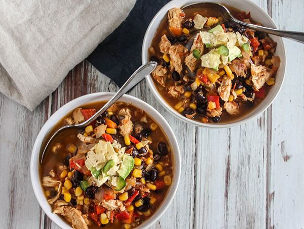 Two bowls of chicken soup with avocados and spoons