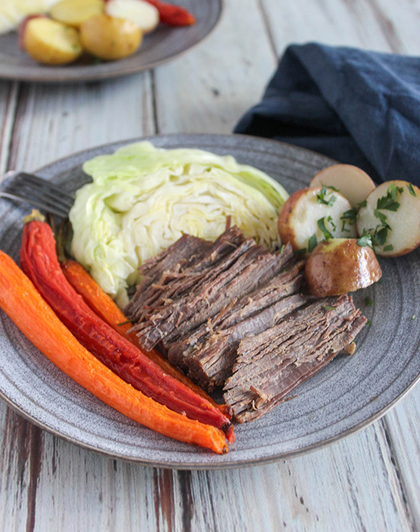 brined corned beef brisked which is brown on a blue plate with carrots potatoes and cabbage