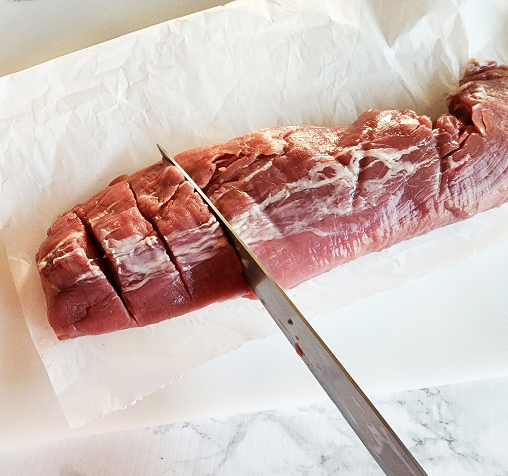 a picture of a knife slicing into a pork tenderloin to make slits about 1 1/2 inches thick