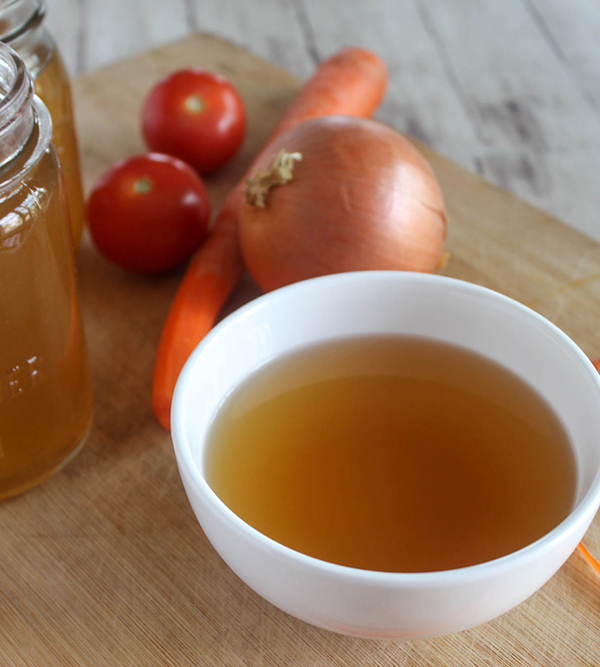 vegetable broth in a bowl with onions and carrots on the side