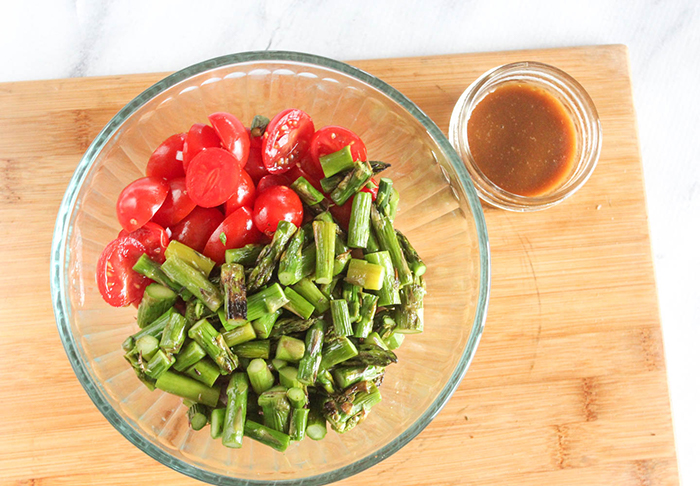 tomatoes and asparagus in a bowl with dressing on the side