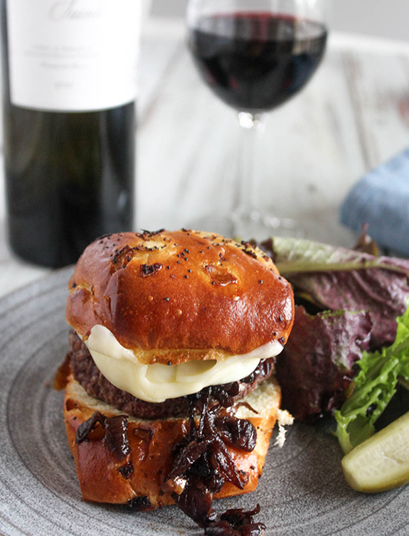 Caramelized onion burger in a roll with a glass of red wine on the side