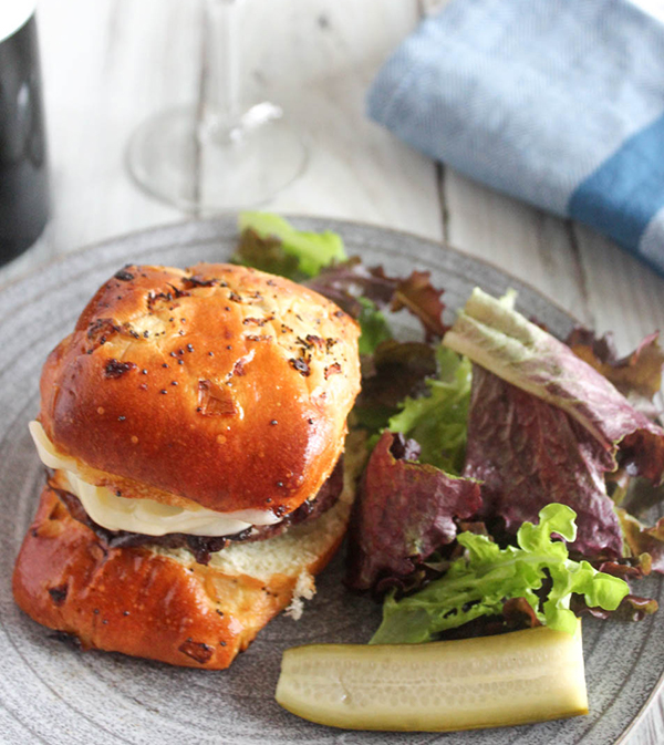 caramelized onion burger on a plate with pickles and a salae