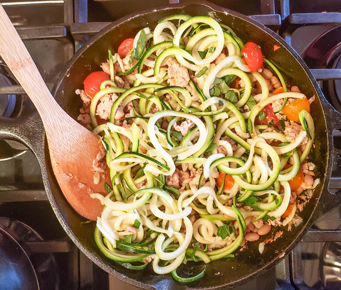 a skillet with zucchini noodles, tomaotes and chicken inpan