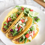 three tacos on plate with lime and lettuce