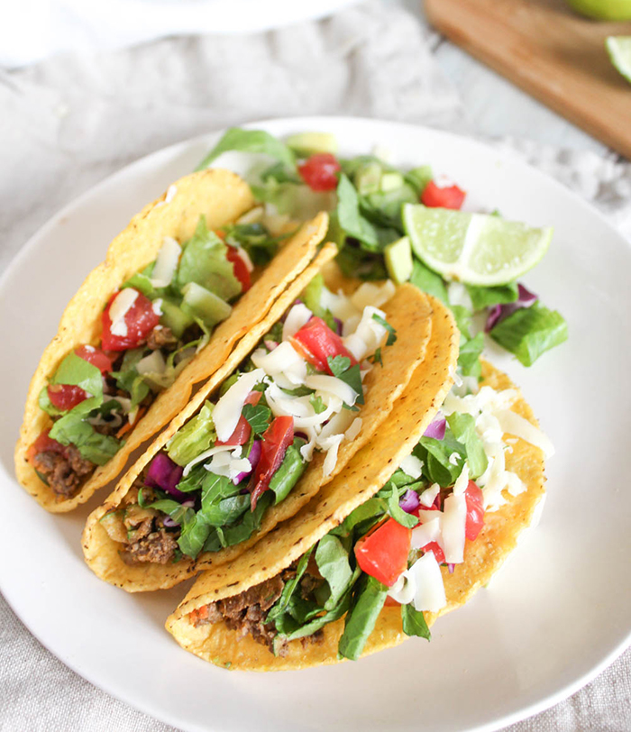 three tacos on plate with lime and lettuce