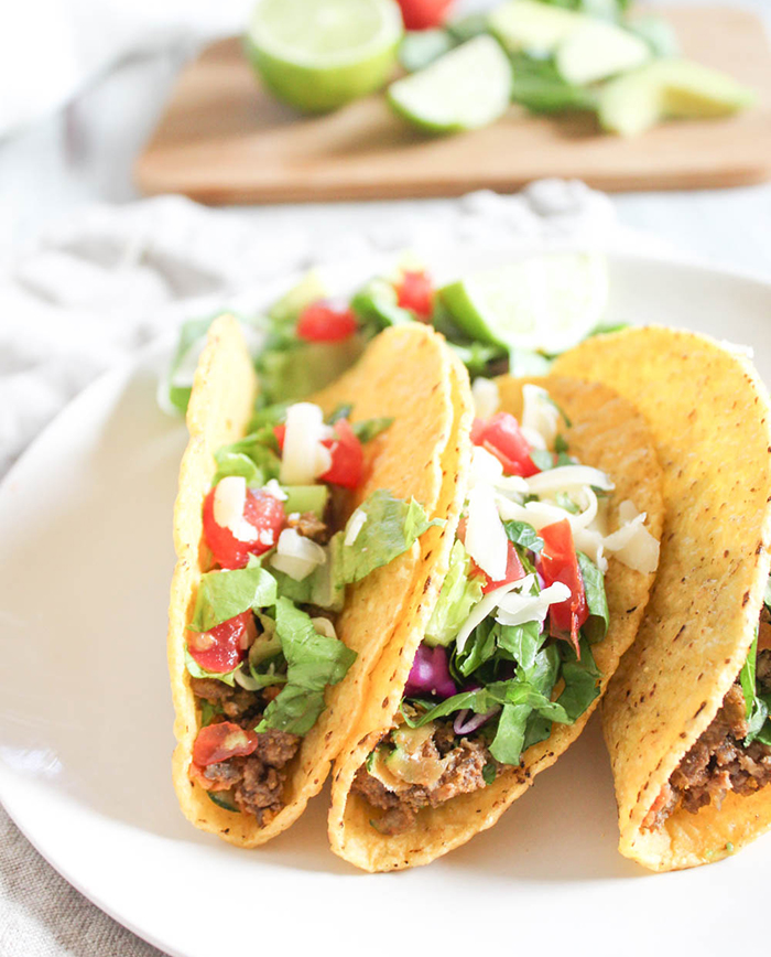 three tacos on a plate with lettuce tomatoes and shredded cheese