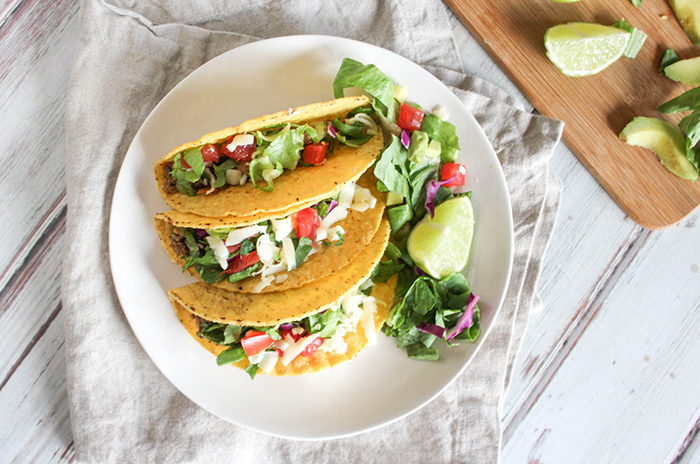 looking down at three tacos on a plate with lettuce and lime