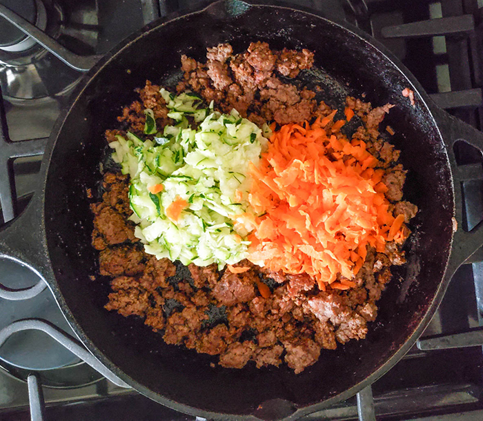 an overhead view of browned beef in a skillet with shredded carrots and onions on top