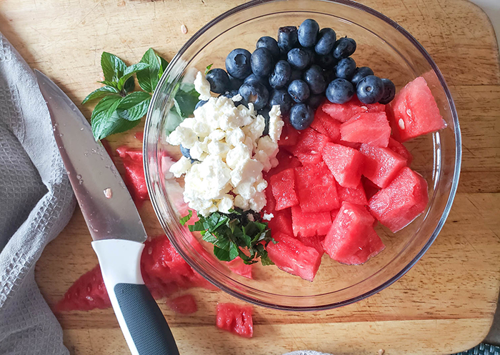 an overhead view of the watermelon salad ingredients (feta cheese, mint, blueberries, watermelon) in a bowl not mixed