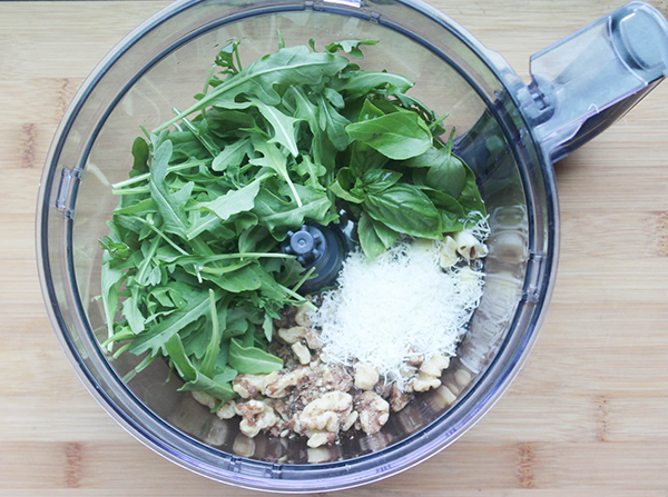 Arugula pesto sauce ingredients in a food processor bowl