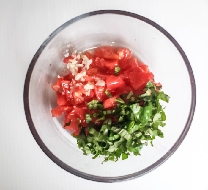 an overhead view of basil, tomatoes and garlic in a bowl