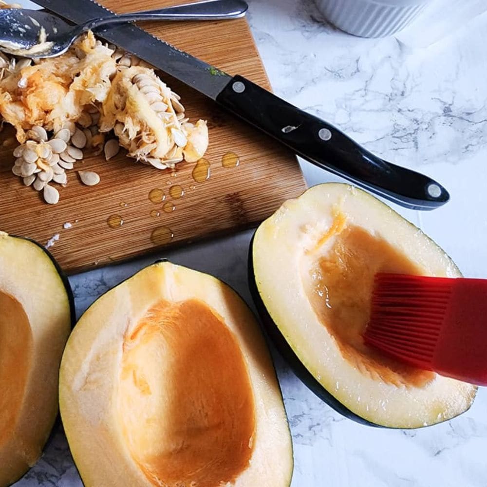 A PICTURE OF A PASTRY BRUSH BRUSING OIL ONTO HALVES OF ACORN SQUASH