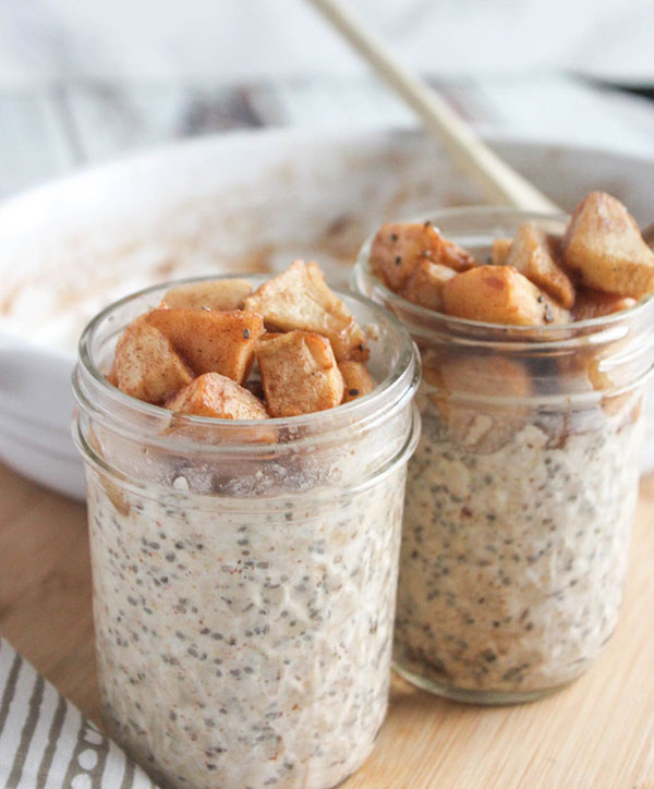 Close up of Apple Cinnamon overnight oats in jars with apples on top ready to serve with empty baking dish in background