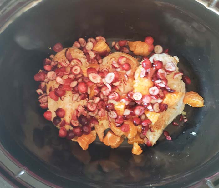 chicken in slow cooker topped with cranberries, oranges