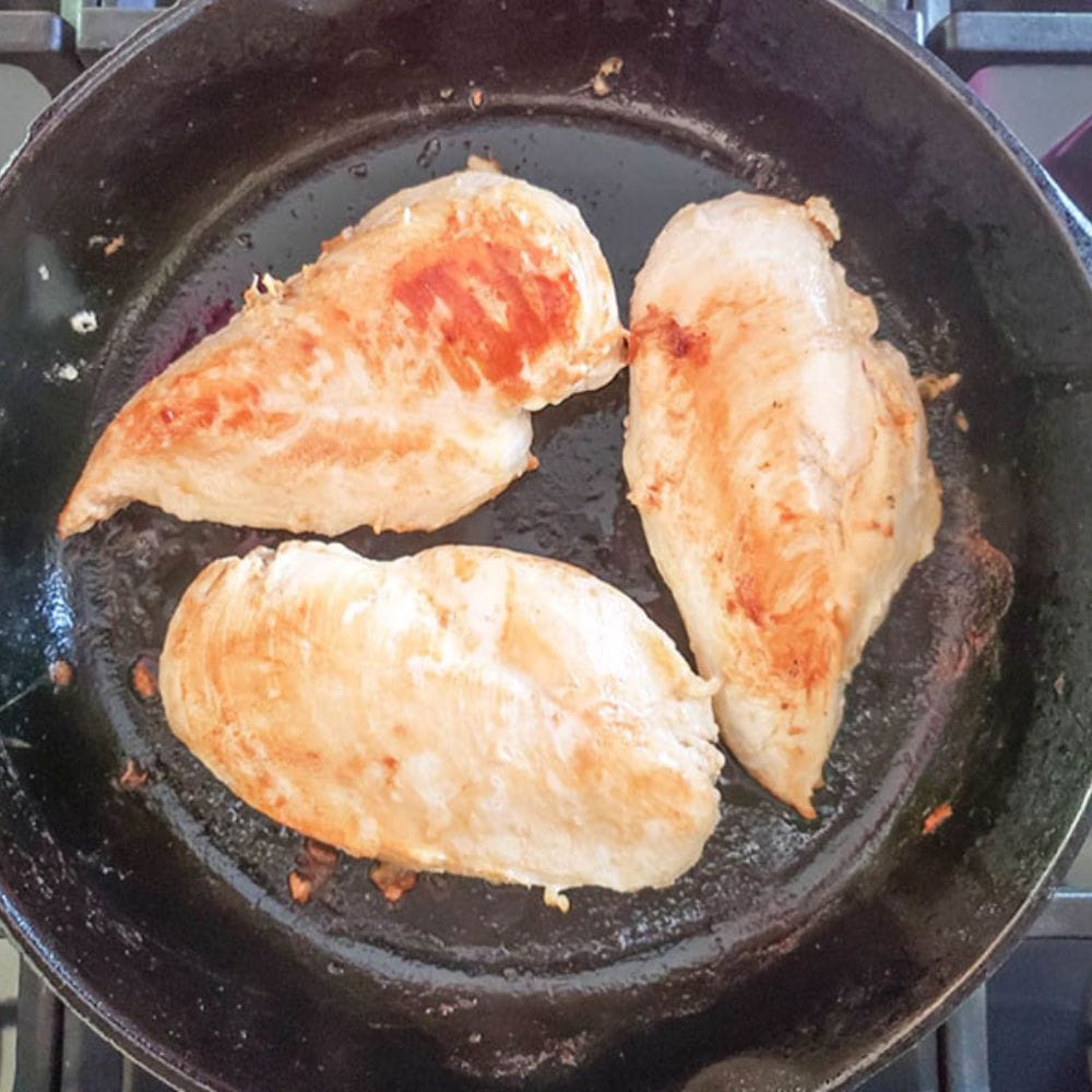 three boneless chicken breasts in a cast iron skillet searing