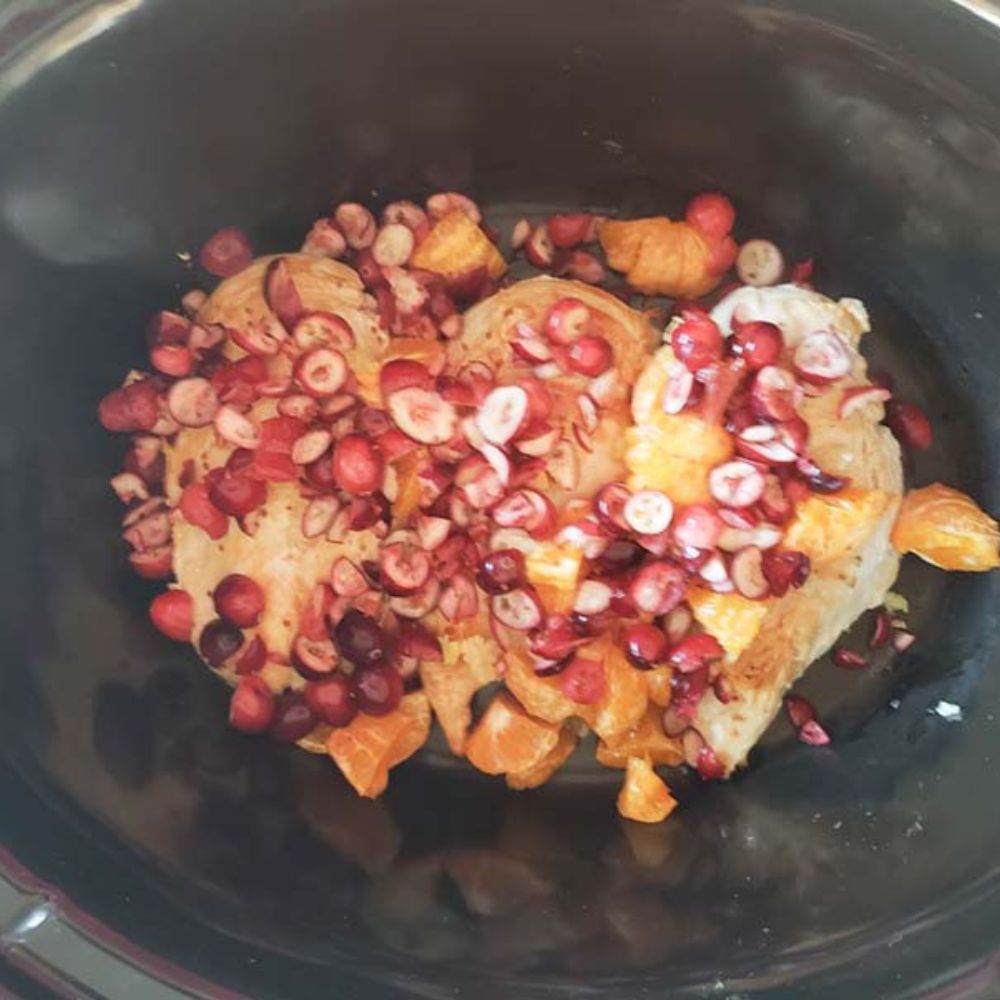 three boneless chicken breasts in a slow cooker with cranberries and sauce added