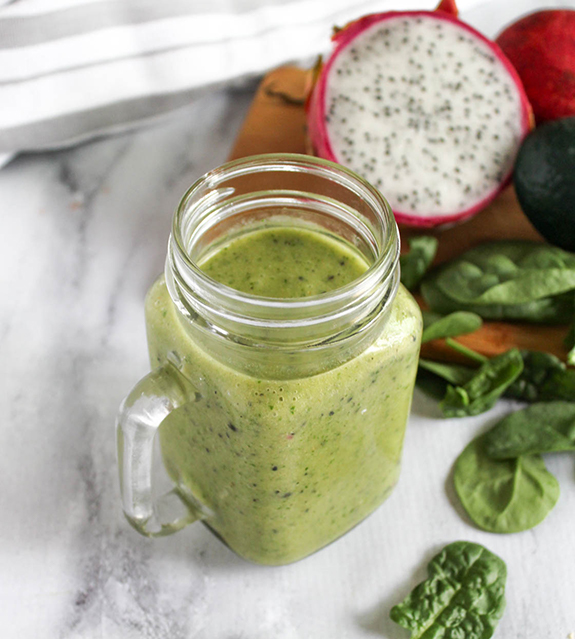 a green smoothie in a glass with dragon fruit in the background