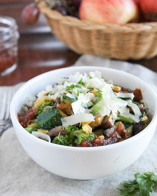 A white bowl full of vegetables, bacon sausage eggs adn cheese