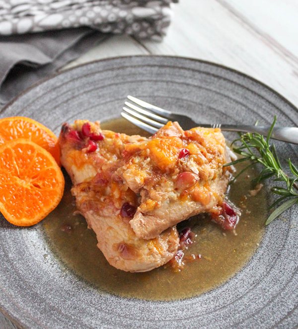 two pieces of chicken in sauce on a plate with orange slices