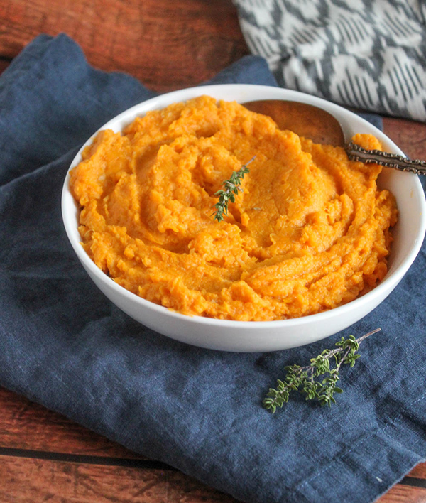 Sweet potatoes mashed in a bowl with a serving spoon