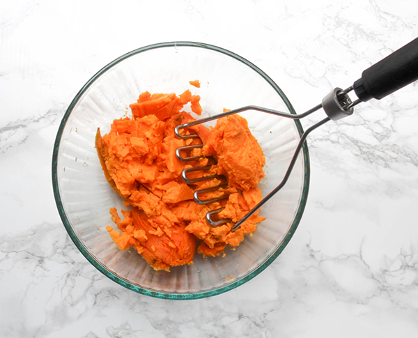 a bowl of sweet potatoes with a potato masher