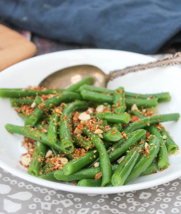 Green beans in a serving bowl topped with bread crumbs and almonds
