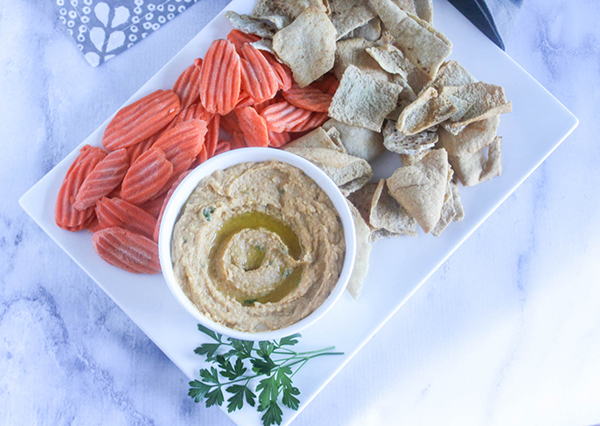 an overhead view of hummus in a bowl with pita chips and carrot chips